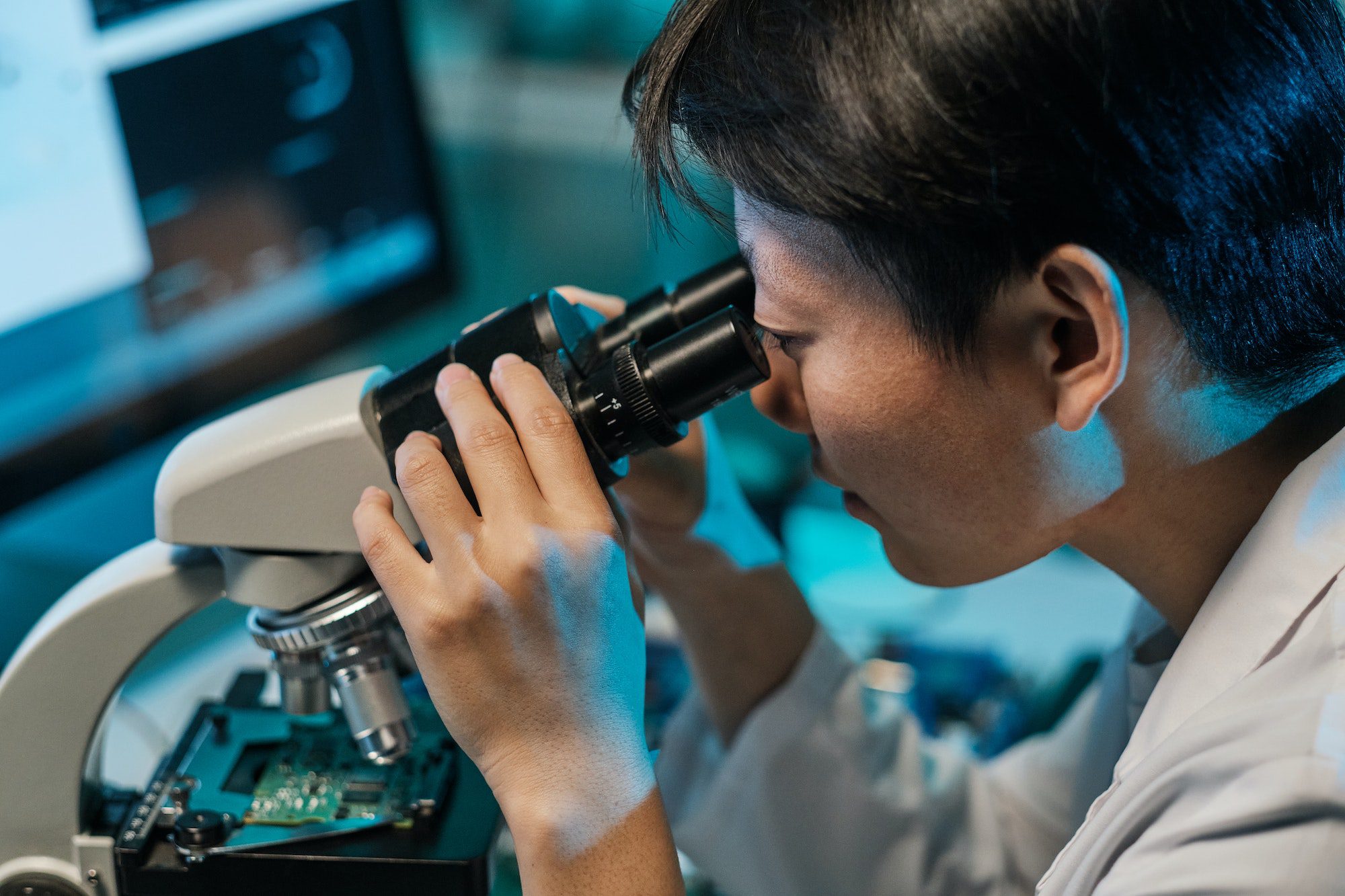 Young Asian technician looking in microscope